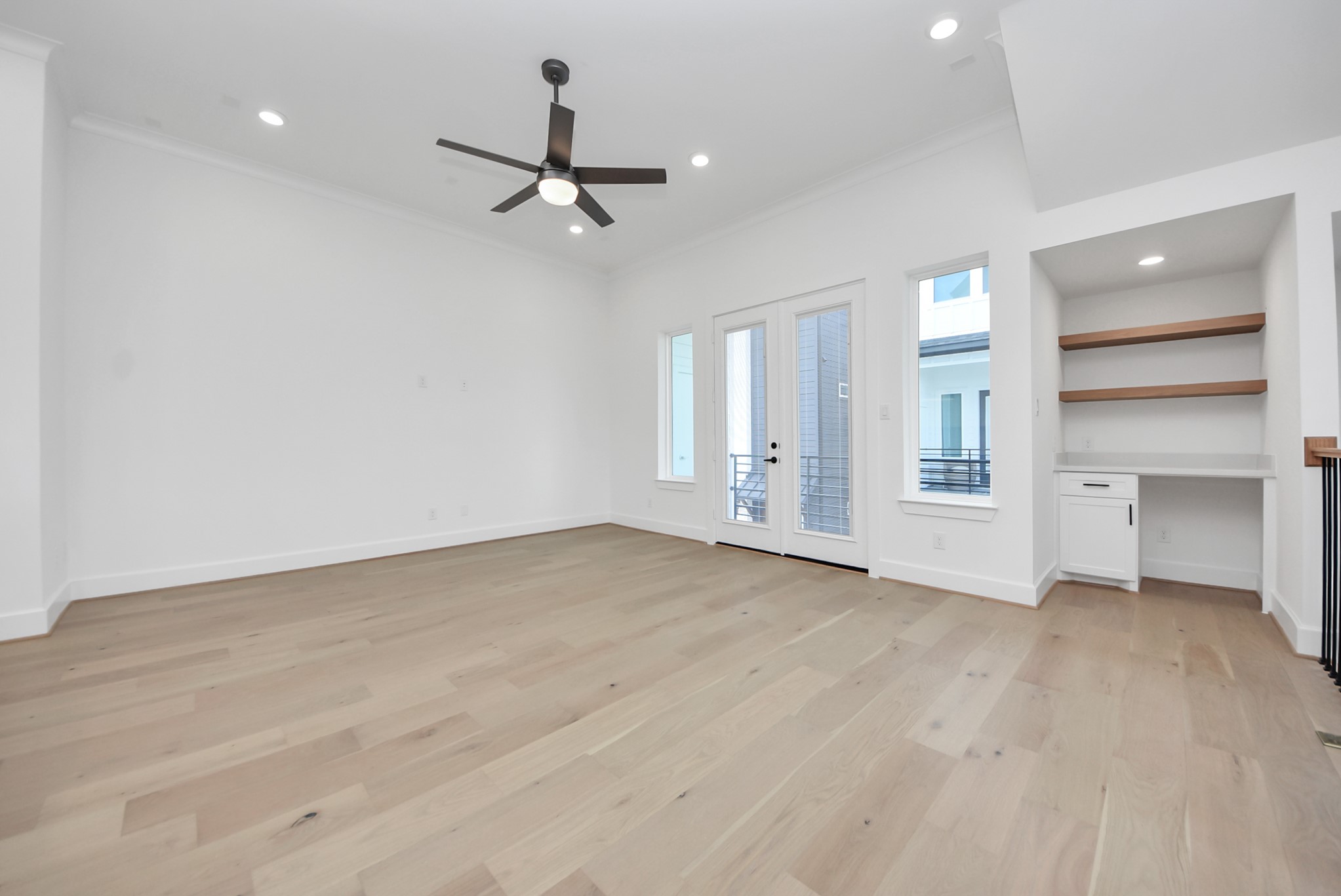 923 Fisher Street, Unit A Houston, TX 77018 - Photo 16 of 47 A light-filled living space featuring warm wood flooring, a modern ceiling fan, and recessed lighting. Double doors open to a private balcony, while a built-in desk with shelving creates a functional home office nook.