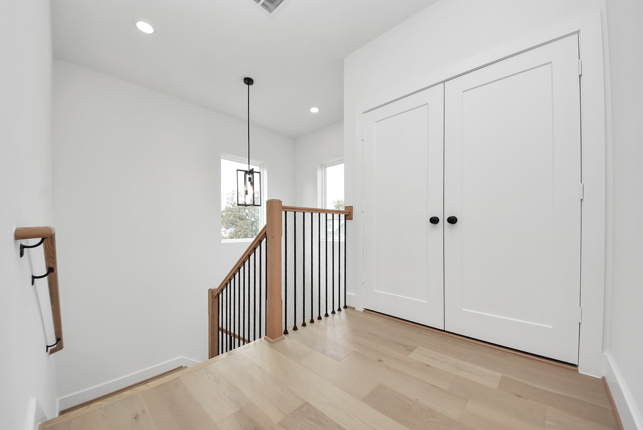 923 Fisher Street, Unit A Houston, TX 77018 - Photo 20 of 47 A bright landing area featuring light wood floors, white walls, and a sleek black metal railing. Pendant lighting, double closet doors, and large windows enhance the open, airy feel.