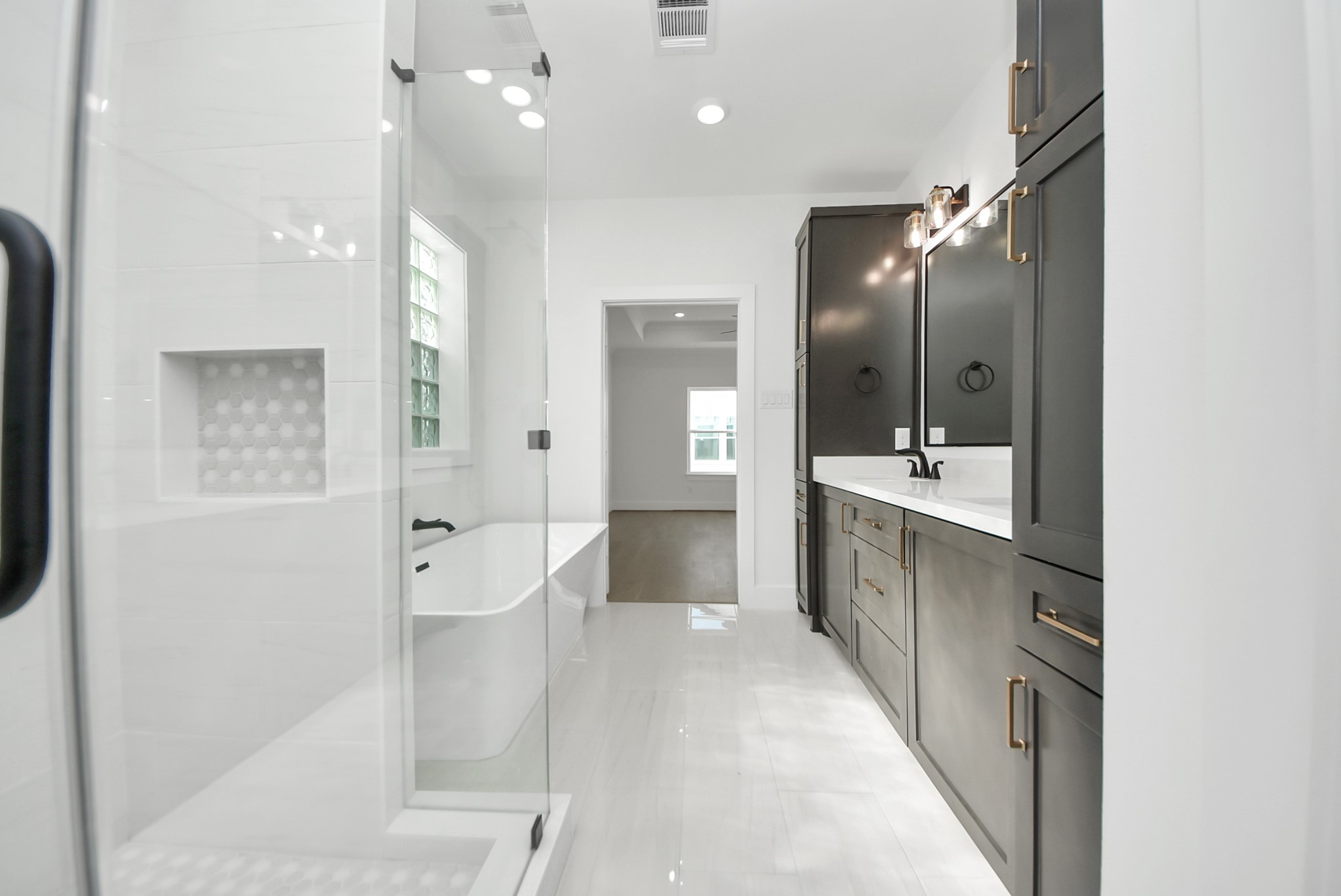 923 Fisher Street, Unit A Houston, TX 77018 - Photo 21 of 47 A modern bathroom showcasing dark cabinetry, sleek fixtures, a glass-enclosed shower, and a separate soaking tub. White walls and natural light from a large window create a bright, spa-like atmosphere.