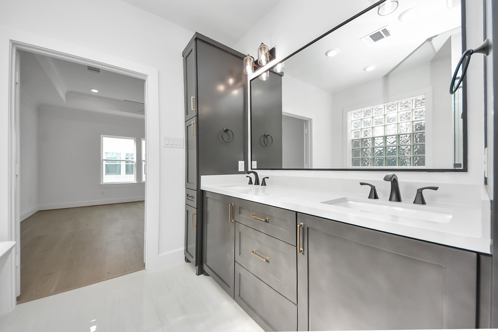 923 Fisher Street, Unit A Houston, TX 77018 - Photo 22 of 47 A contemporary bathroom with a double vanity featuring dark cabinetry and a large mirror. Glass block windows provide natural light and privacy, while the layout opens seamlessly to a spacious, light-filled bedroom.