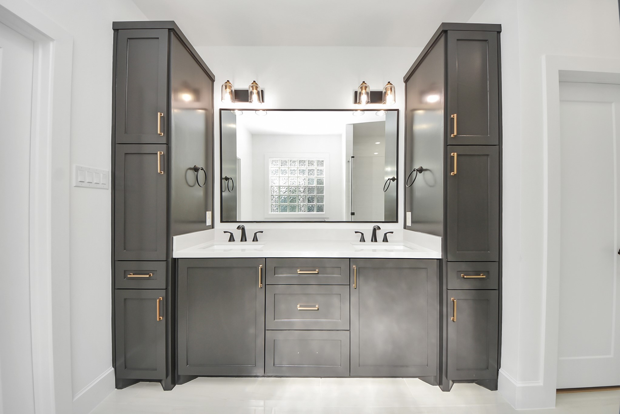 923 Fisher Street, Unit A Houston, TX 77018 - Photo 23 of 47 A sleek bathroom design highlighted by a modern double vanity with dark cabinetry and gold hardware. A large mirror and overhead lighting illuminate the space, balanced by clean white walls and countertops.