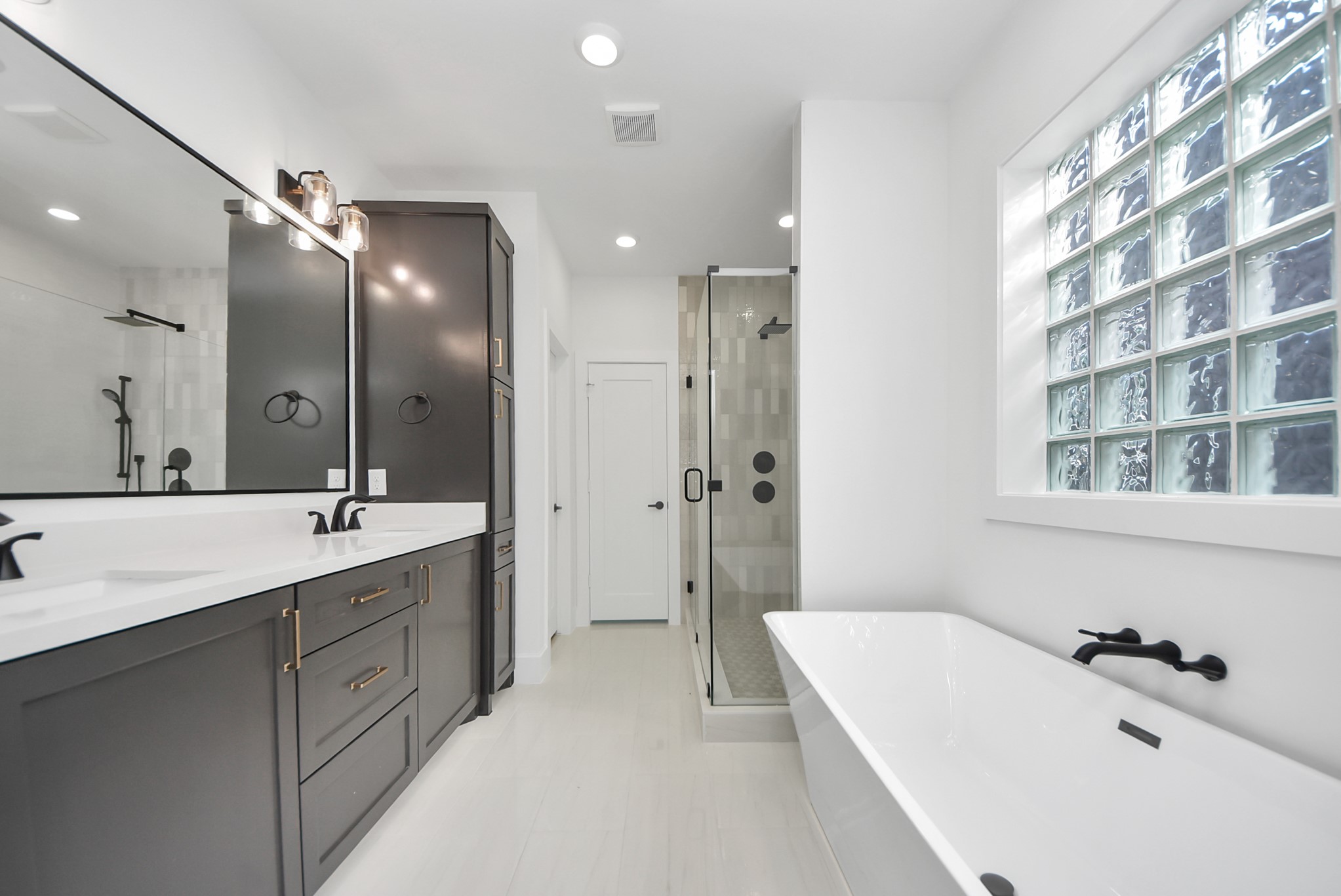 923 Fisher Street, Unit A Houston, TX 77018 - Photo 25 of 47 A spa-inspired bathroom with a sleek double vanity, expansive mirror, and generous storage. A glass-enclosed shower, freestanding tub, and glass block windows allow natural light to enhance the airy, modern design.