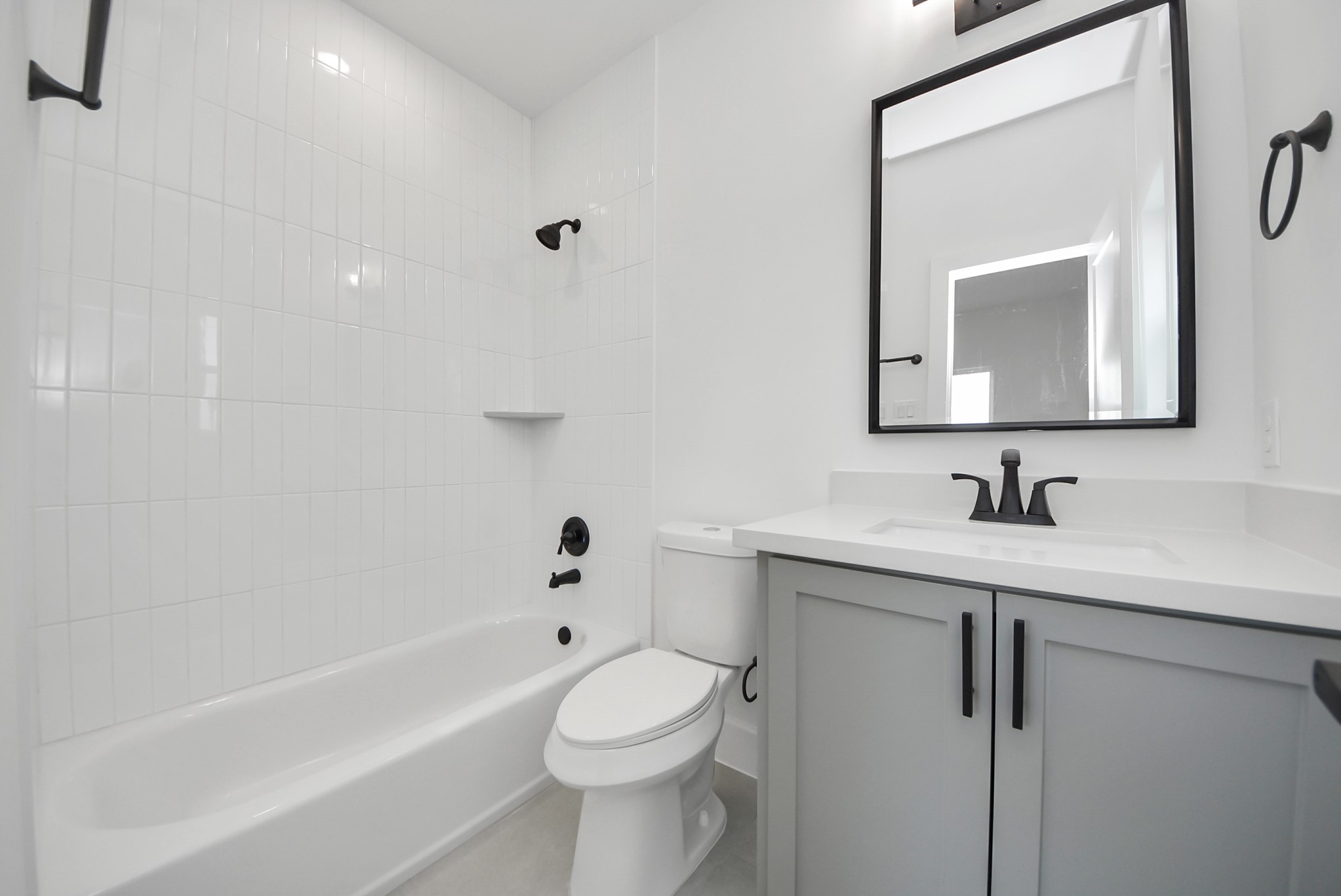 923 Fisher Street, Unit A Houston, TX 77018 - Photo 36 of 47 The main bathroom offers a clean, modern design with a white tiled shower, a bathtub, and a sleek vanity with large mirror. Black fixtures add contemporary elegance while the space remains bright and airy.