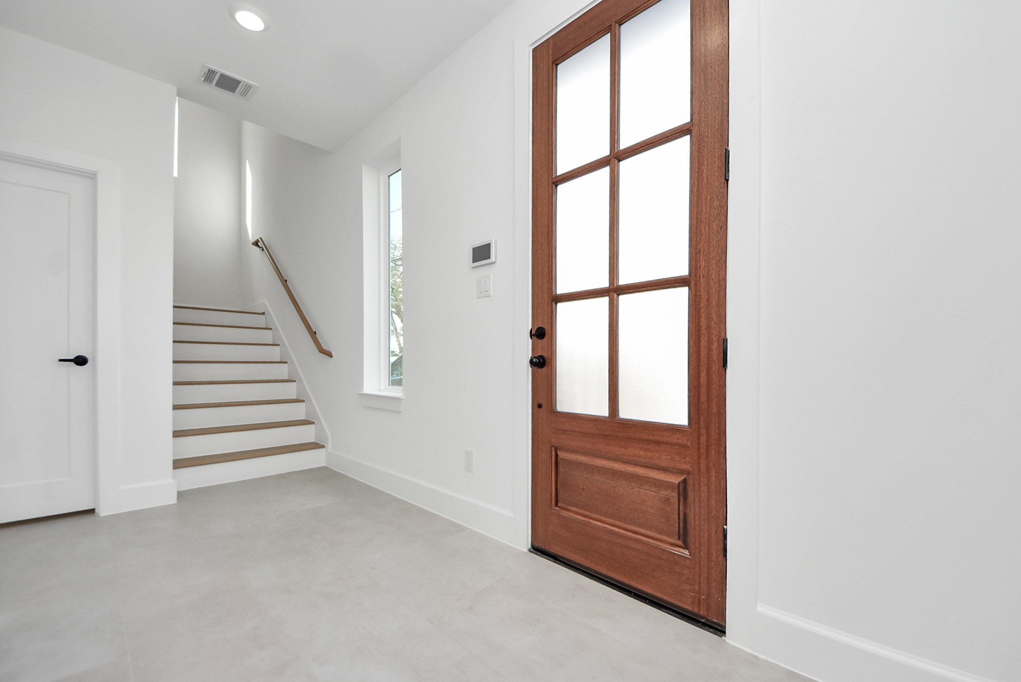923 Fisher Street, Unit A Houston, TX 77018 - Photo 5 of 47 A bright, modern entryway featuring a wood front door with glass panels that allow natural light to flow throughout the space. Neutral walls, light tile flooring, and a staircase with a clean wood handrail set a polished, contemporary tone upon entry.