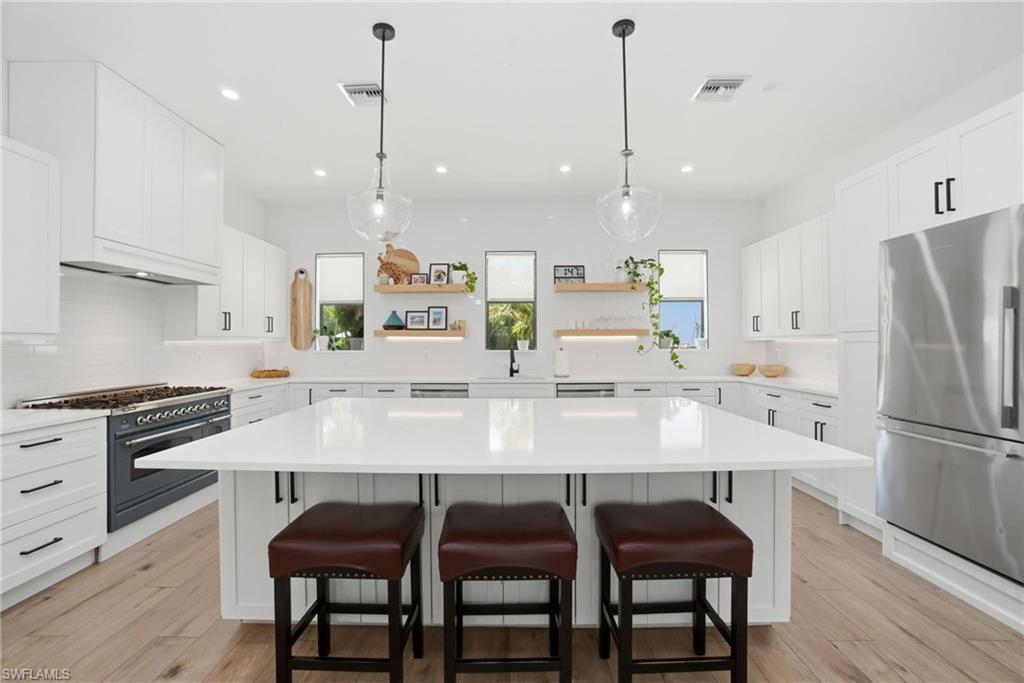 522 31st Street Southwest Naples, FL 34117 - Photo 13 of 38 Spacious kitchen featuring an expansive central island, white cabinetry with black hardware, stainless steel appliances, wood-finish flooring, and pendant lighting