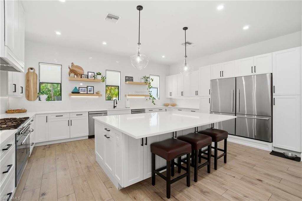 522 31st Street Southwest Naples, FL 34117 - Photo 14 of 38 Spacious kitchen featuring an expansive central island with seating, white shaker cabinetry, stainless steel appliances, and light wood-finish flooring