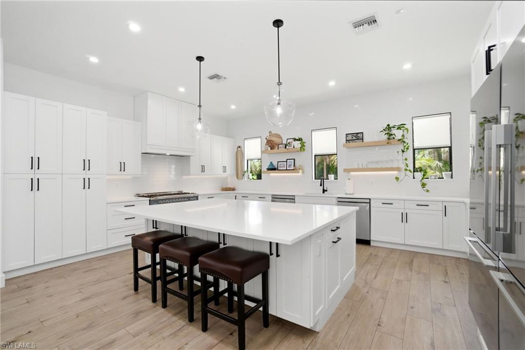 522 31st Street Southwest Naples, FL 34117 - Photo 15 of 38 Spacious kitchen featuring an expansive central island with seating, extensive white cabinetry, light wood-finish flooring, recessed lighting, and stainless steel appliances