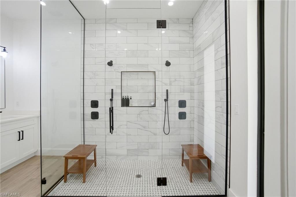 522 31st Street Southwest Naples, FL 34117 - Photo 23 of 38 Spacious walk-in shower featuring a glass enclosure with matte black trim, white subway tile walls, a mosaic tile floor, dual shower heads, and an integrated shower niche