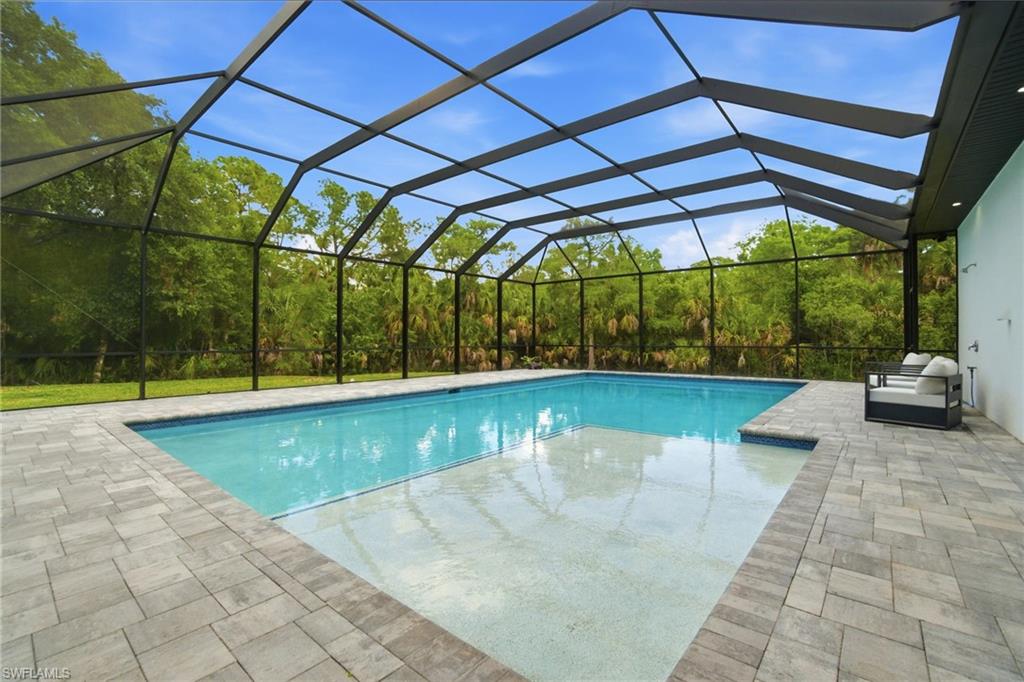 522 31st Street Southwest Naples, FL 34117 - Photo 38 of 38 Screened-in swimming pool featuring a paver patio surround, integrated sun shelf, and a perimeter of mature trees beyond the enclosure
