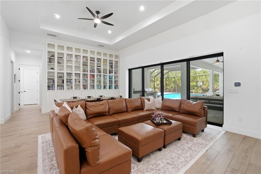 522 31st Street Southwest Naples, FL 34117 - Photo 8 of 38 Spacious living area featuring light wood-finish flooring, a tray ceiling with recessed lighting and a ceiling fan, and extensive built-in shelving with glass-front cabinets