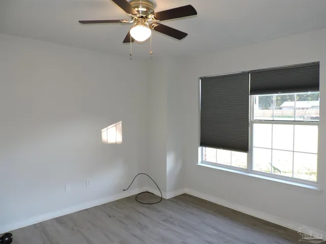 an empty room with wooden floor fan and windows