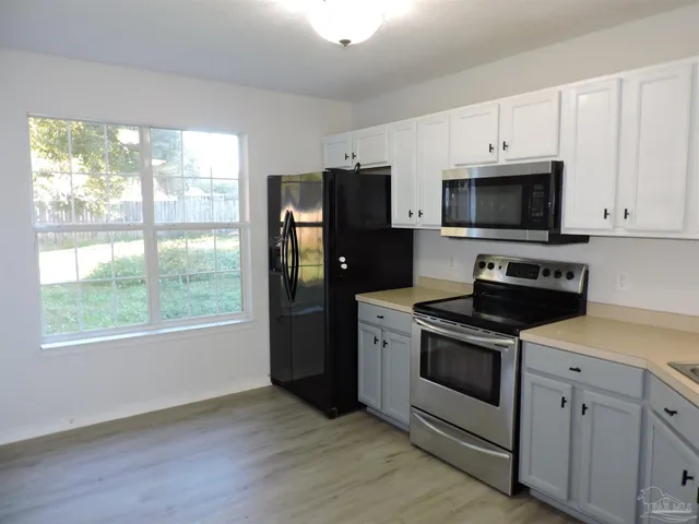 a kitchen with stainless steel appliances granite countertop a stove a microwave a refrigerator a sink and white cabinets with wooden floor