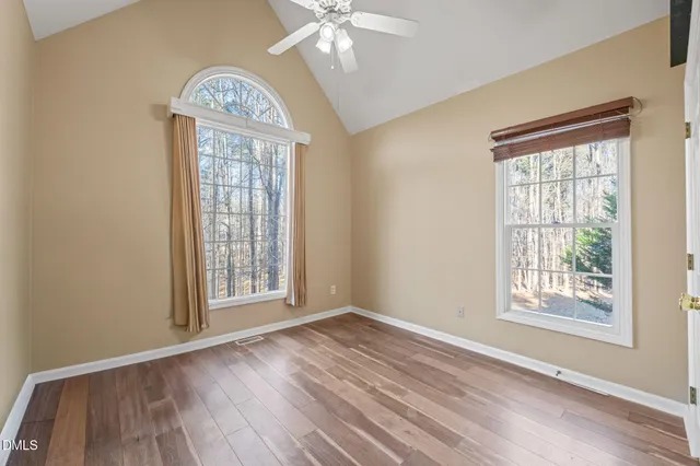 an empty room with wooden floor fan and windows