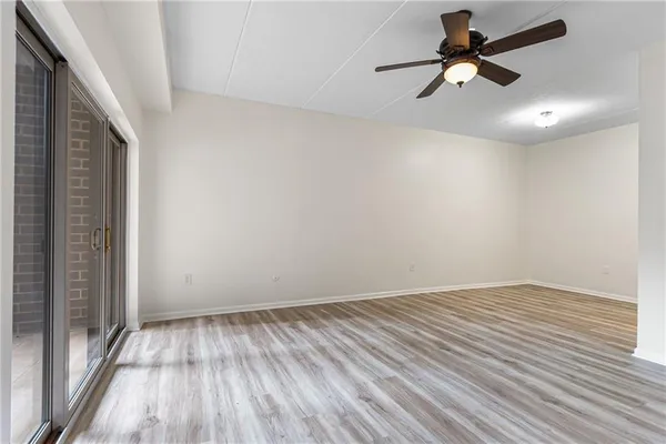 an empty room with wooden floor and way to kitchen