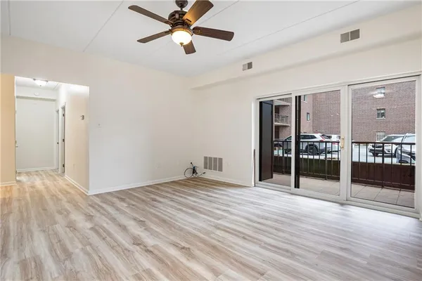 a view of an empty room with wooden floor and a ceiling fan