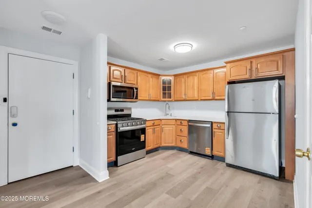 a kitchen with granite countertop stainless steel appliances a refrigerator cabinets wooden floor and a window