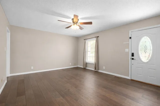 an empty room with wooden floor fan and windows