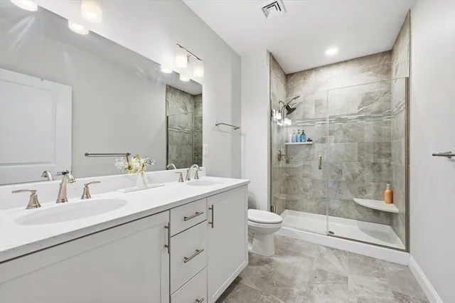 a bathroom with a double vanity sink toilet mirror and shower