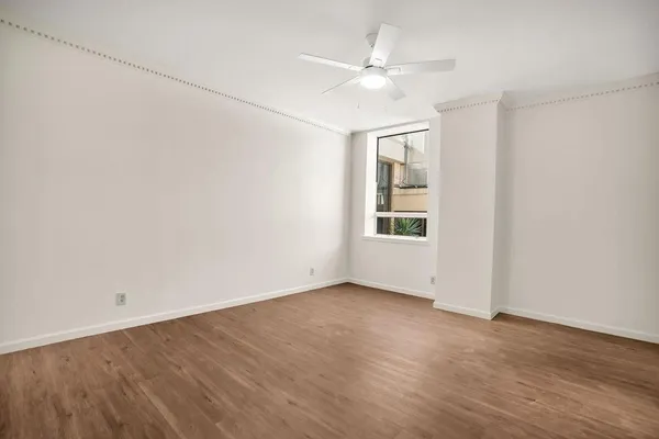an empty room with wooden floor chandelier fan and windows