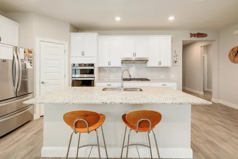 a kitchen with stainless steel appliances granite countertop a sink a stove a refrigerator with a dining table and chairs