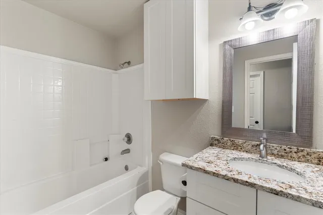 a bathroom with a granite countertop sink a toilet and bathtub
