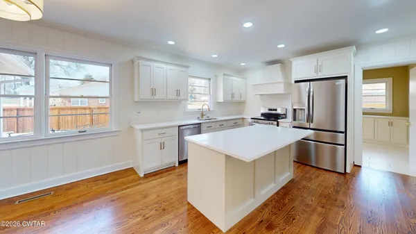 a kitchen with stainless steel appliances a refrigerator a sink dishwasher a stove and white cabinets with wooden floor