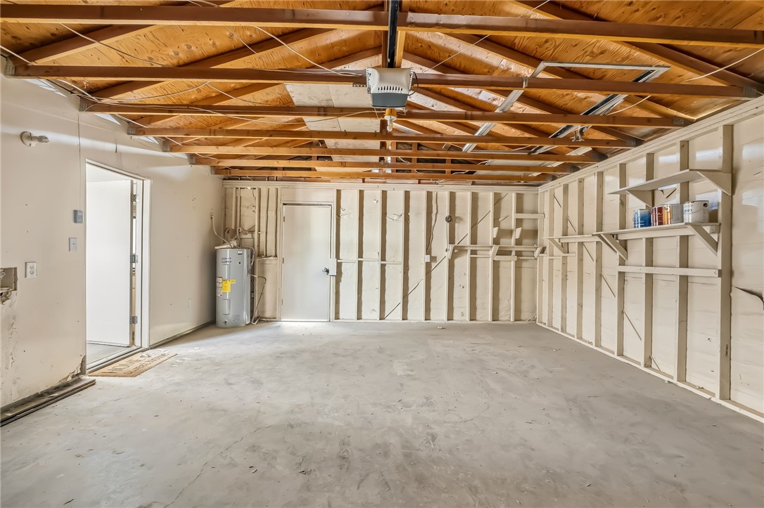 1720 Valencia Road Fort Mohave, AZ 86426 - Photo 7 of 32 Spacious garage featuring exposed wood ceiling beams, concrete flooring, built-in shelving, a water heater, and a garage door opener