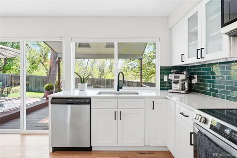 a kitchen with granite countertop a stove a sink and white cabinets with wooden floors