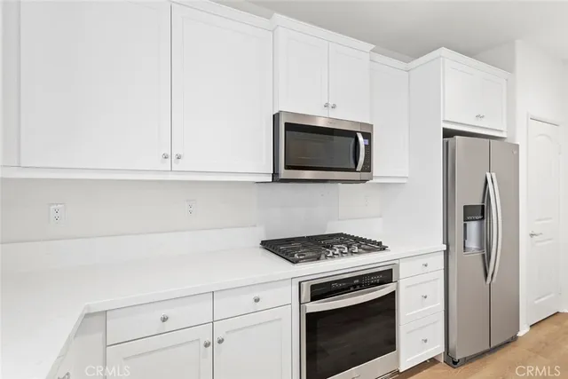 a kitchen with stainless steel appliances white cabinets and a stove a refrigerator with wooden floor