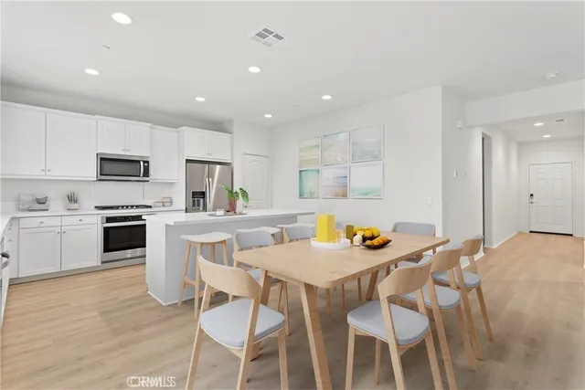 a kitchen with stainless steel appliances kitchen island granite countertop a dining table chairs stove refrigerator and cabinets