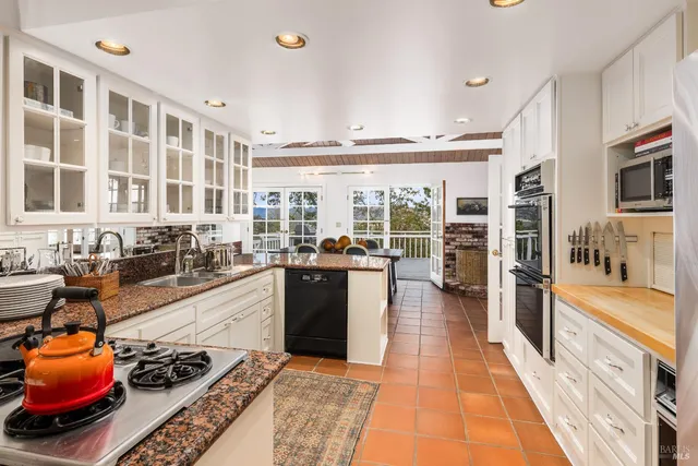 a large white kitchen with stainless steel appliances granite countertop a stove and a large window