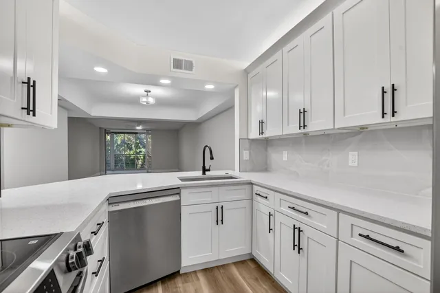 a kitchen with a sink dishwasher and white cabinets with wooden floor