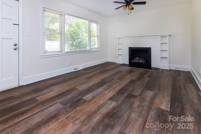 an empty room with wooden floor fireplace and windows