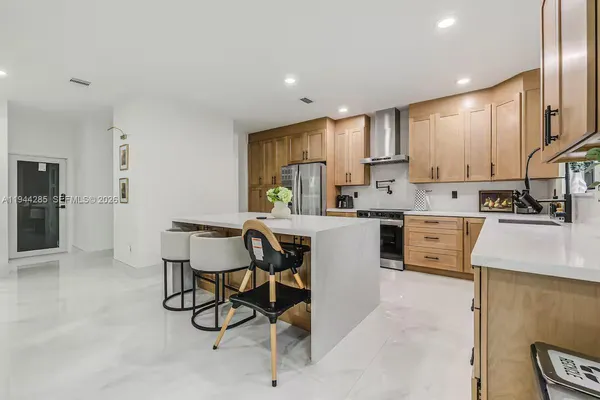 a kitchen with stainless steel appliances kitchen island granite countertop a stove a sink a refrigerator white cabinets and chairs with wooden floor