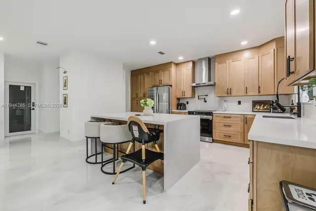 a kitchen with stainless steel appliances kitchen island granite countertop a stove a sink a refrigerator white cabinets and chairs with wooden floor