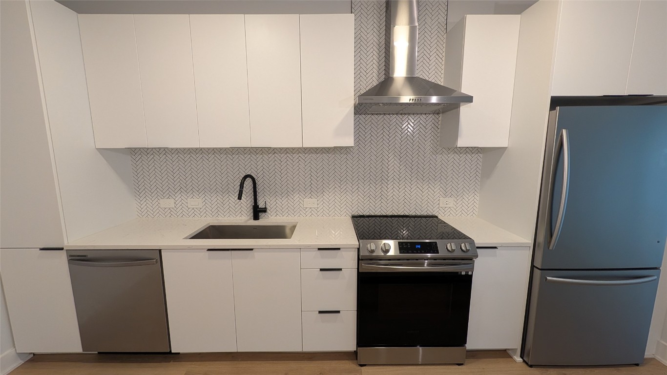 2500 Longview Street, Unit 218 Austin, TX 78705 - Photo 9 of 19 Kitchen with modern cabinets, stainless steel appliances, wall chimney range hood, white cabinetry, and decorative backsplash