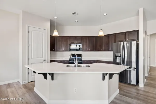 a kitchen with stainless steel appliances granite countertop a sink a stove a refrigerator and island with wooden floor