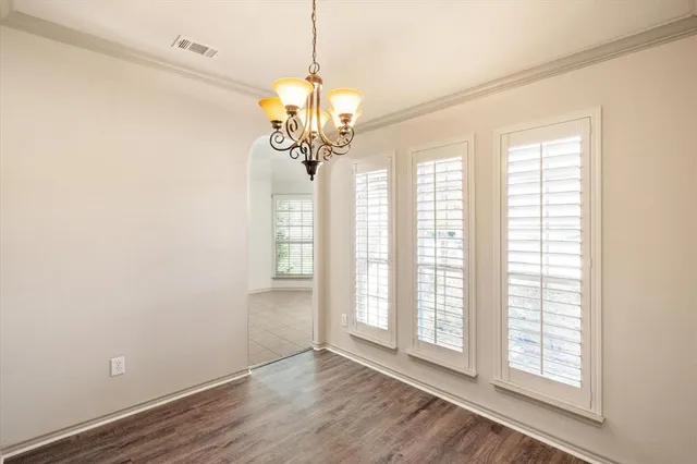an empty room with wooden floor chandelier and windows