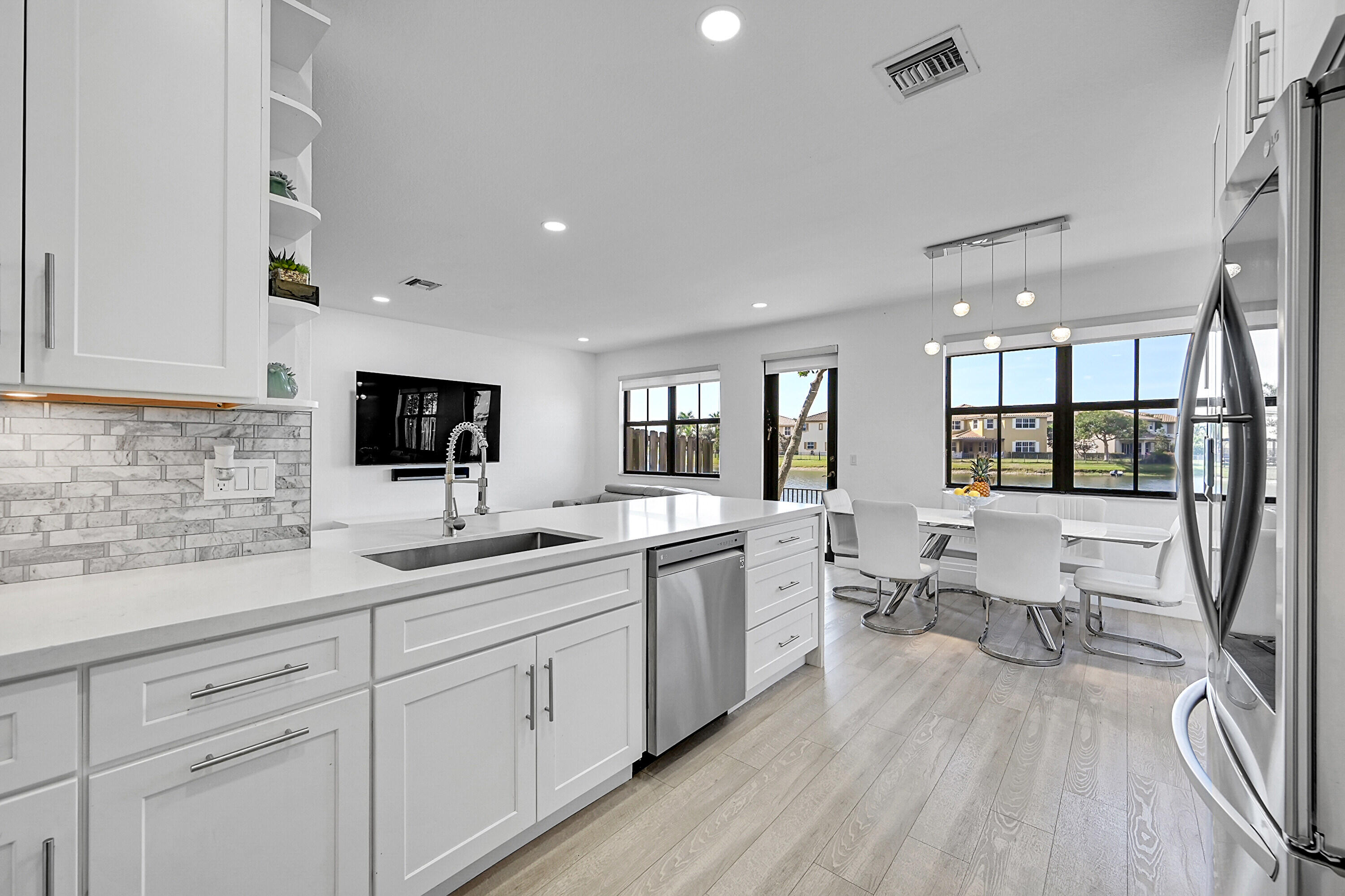 8459 Lakeview Trail Parkland, FL 33076 - Photo 18 of 55 a open kitchen with white cabinets a sink dishwasher a dining table and chairs with wooden floor