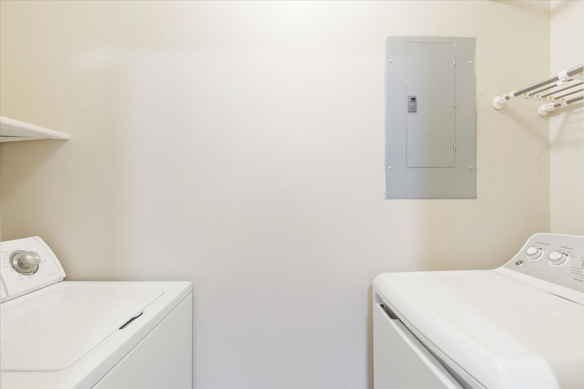 3502 Ocee Street, Unit 3502 Houston, TX 77063 - Photo 7 of 28 This photo shows a compact laundry room with a washer, dryer, and shelving. The space features a utility panel on the wall and a hanging rod for convenience.
