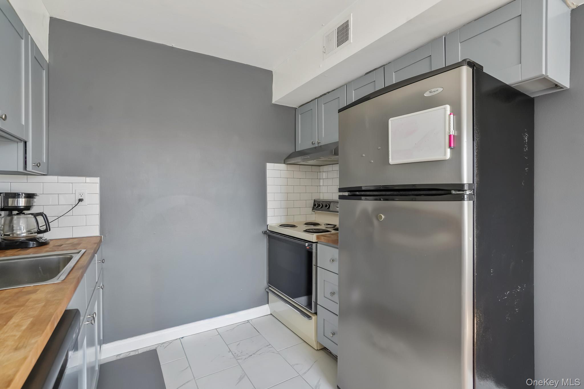 26 Cooper Road, Unit 411 Poughkeepsie, NY 12603 - Photo 8 of 17 Kitchen with gray cabinets, freestanding refrigerator, white range with electric cooktop, and tasteful backsplash