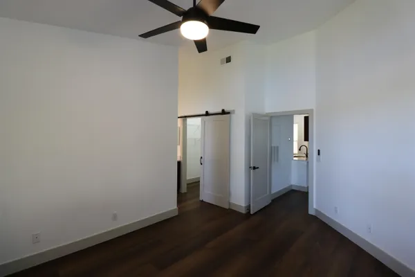 an empty room with wooden floor a ceiling fan and kitchen space