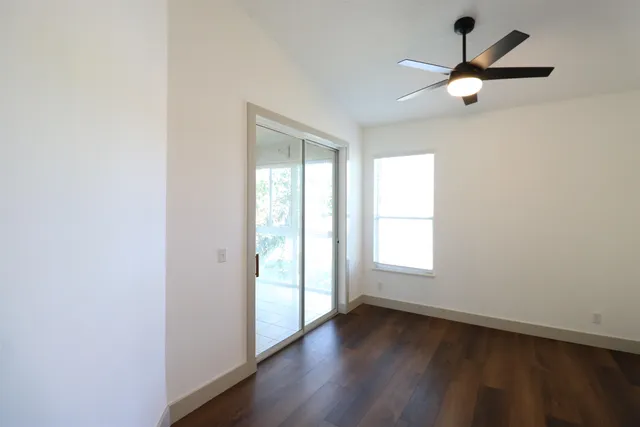 an empty room with wooden floor fan and windows