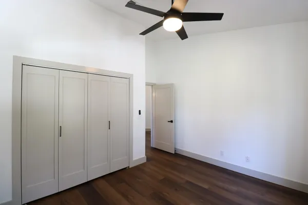 an empty room with wooden floor closet fan and windows