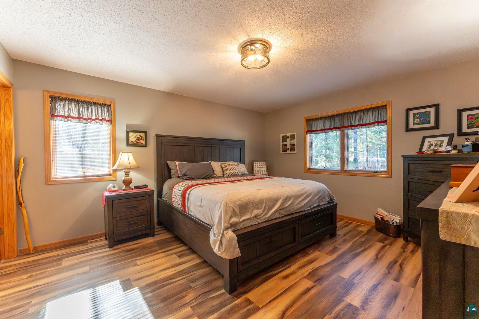 4452 Moccasin Point Road Tower, MN 55790 - Photo 12 of 44 Bedroom featuring wood-finish flooring, two windows with wood trim, a ceiling-mounted light fixture, and neutral-toned wall paint