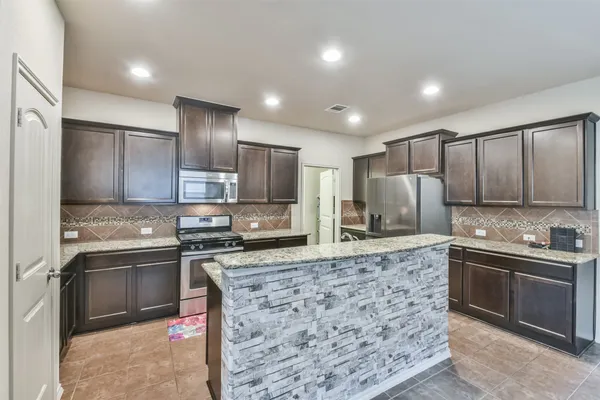 a kitchen with stainless steel appliances kitchen island granite countertop a sink stove refrigerator and cabinets