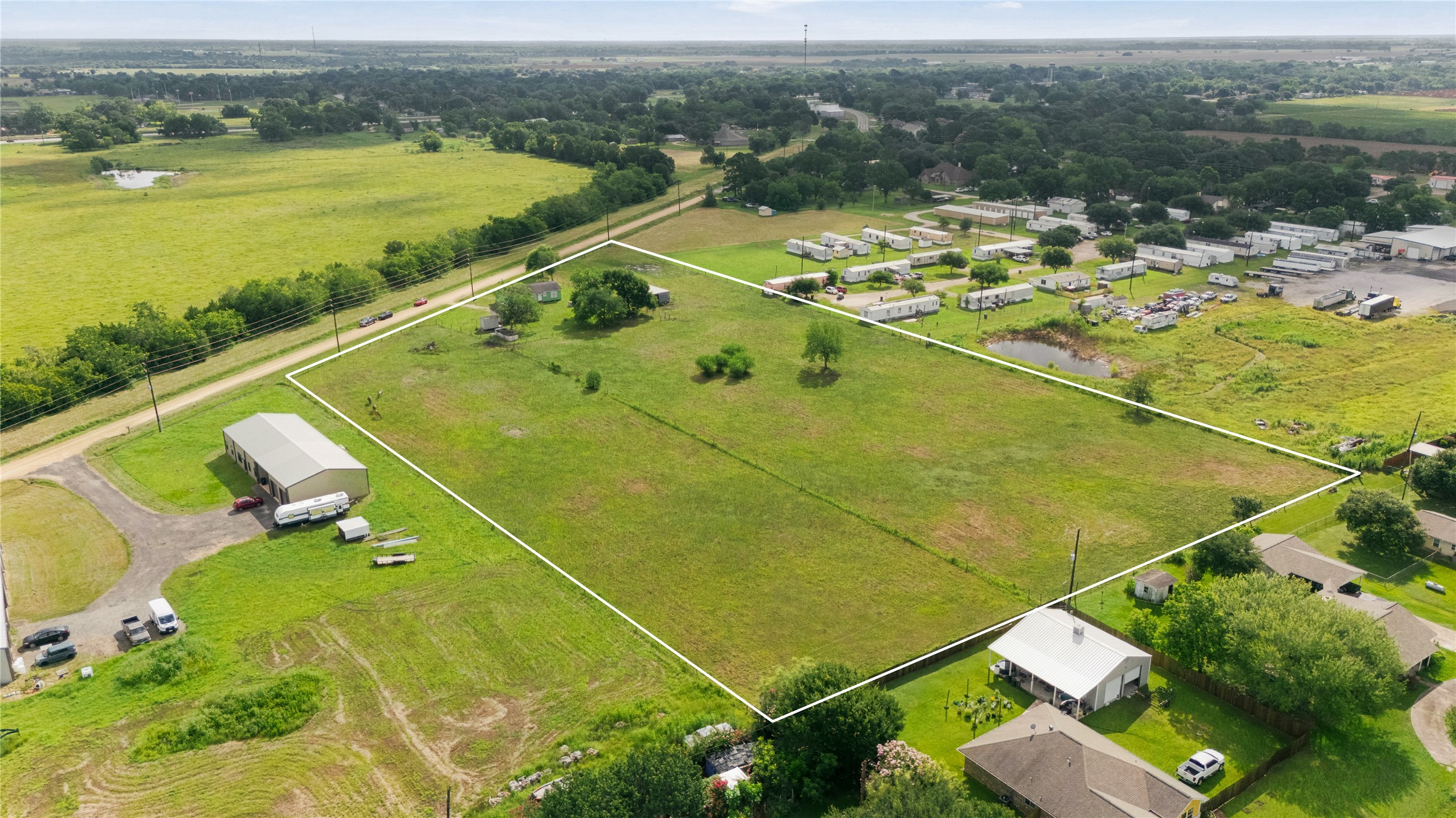 765 Norcross Road Wallis, TX 77485 - Photo 40 of 42 The photo shows an outline of the entire tract of 6 plus acres of spacious rural property with open green fields, a large outbuilding, and a few homes nearby. It offers a peaceful setting with plenty of space and a nearby road for easy access.