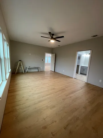 an empty room with chandelier fan and windows