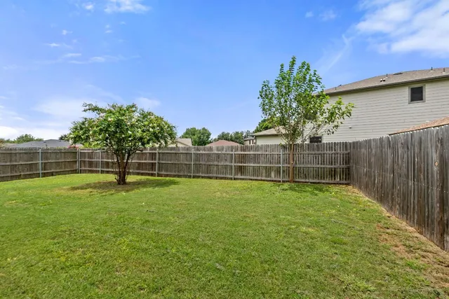 a view of a backyard with large trees and wooden fence