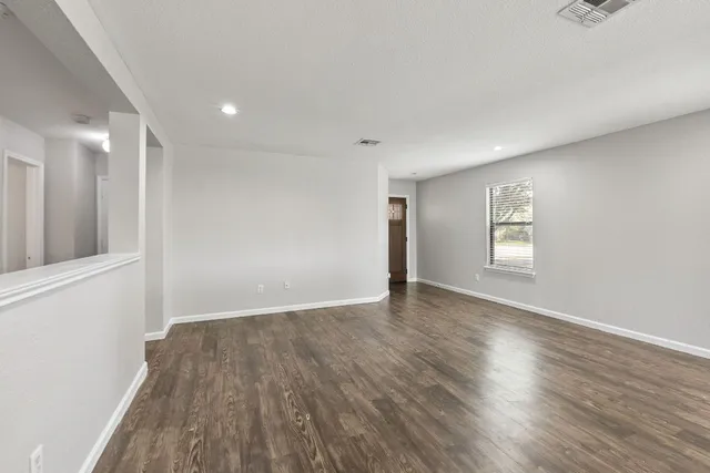 a view of an empty room with wooden floor and a window